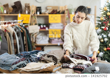 Uncertain young Armenian girl choosing sweater in clothing store Uncertain young Armenian girl choosing sweater in clothing store 141925702