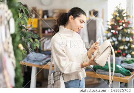 Armenian woman stands in a shop decorated for Christmas and chooses a handbag Armenian woman stands in a shop decorated for Christmas and chooses a handbag 141925703
