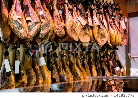 Row of dangling legs jamon with labels on showcase of butcher shop Row of dangling legs jamon with labels on showcase of butcher shop 141925772