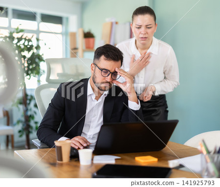 Man and woman working in office looking sadly at laptop Man and woman working in office looking sadly at laptop 141925793