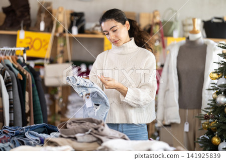 Uncertain young Armenian girl choosing jeans pantaloons in clothing store Uncertain young Armenian girl choosing jeans pantaloons in clothing store 141925839