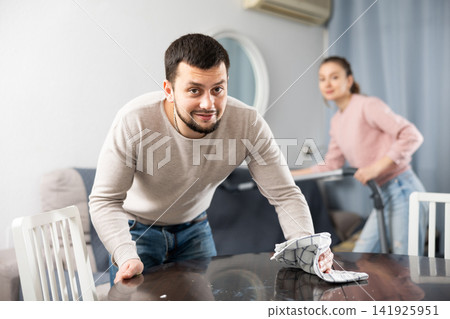 Guy rubbing wooden furniture while wife vacuuming sofa Guy rubbing wooden furniture while wife vacuuming sofa 141925951