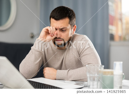 Young man rubbing tired eyes while working on computer at home Young man rubbing tired eyes while working on computer at home 141925985