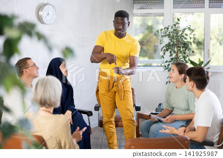 Group of multinational people have discussion while sitting on chairs in circle Group of multinational people have discussion while sitting on chairs in circle 141925987