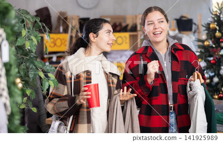 Two girls with cup of coffee talking during shopping in womens clothing store Two girls with cup of coffee talking during shopping in womens clothing store 141925989