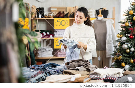 Armenian woman stands against the background of a Christmas tree and chooses denim pants Armenian woman stands against the background of a Christmas tree and chooses denim pants 141925994