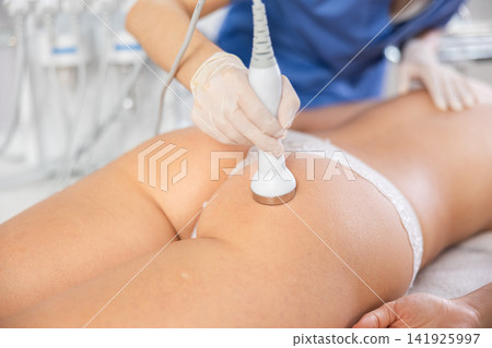 Cosmetologist performing high-frequency ultrasound procedure on female buttocks 141925997