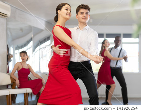 Pretty young woman dancing waltz with partner at group of multinational people in ballroom dancing class Pretty young woman dancing waltz with partner at group of multinational people in ballroom dancing class 141926254