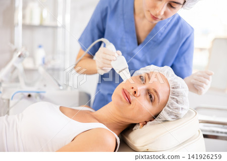 Young woman cosmetologist doing exfoliation procedure to young woman Young woman cosmetologist doing exfoliation procedure to young woman 141926259