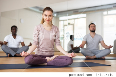 Woman sitting in lotus pose doing yoga meditation with group Woman sitting in lotus pose doing yoga meditation with group 141926410