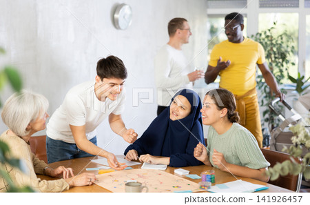 Excited young guy playing board game at table with friends Excited young guy playing board game at table with friends 141926457