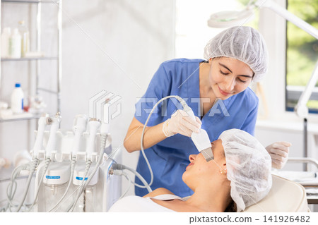 Female cosmetologist performing facial cleansing with ultrasonic shovel on woman Female cosmetologist performing facial cleansing with ultrasonic shovel on woman 141926482