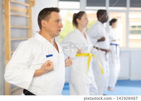 Women and men in kimono in fight stance during group karate training Women and men in kimono in fight stance during group karate training 141926487