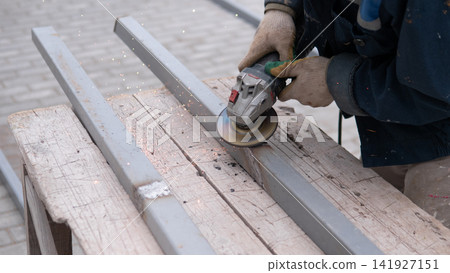 Close up of gloved worker cutting or grinding steel beams on rough wooden bench, with bright sparks flying across outdoor workspace, showing hands on fabrication, repair, construction, and Close up of gloved worker cutting or grinding steel beams on rough wooden bench, with bright sparks flying across outdoor workspace, showing hands on fabrication, repair, construction, and 141927151