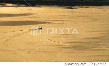 The surface of Lake Biwa, shining golden in the morning sun, and the silhouette of a fishing boat. The surface of Lake Biwa, shining golden in the morning sun, and the silhouette of a fishing boat. 141927434