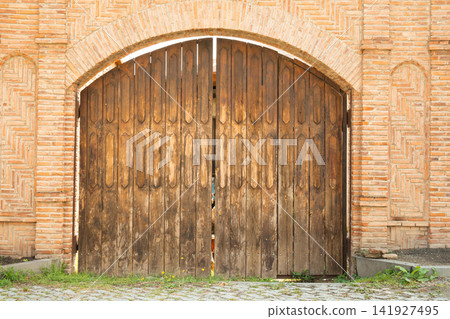Wooden gates stand closed against a backdrop of rustic brick walls Wooden gates stand closed against a backdrop of rustic brick walls 141927495