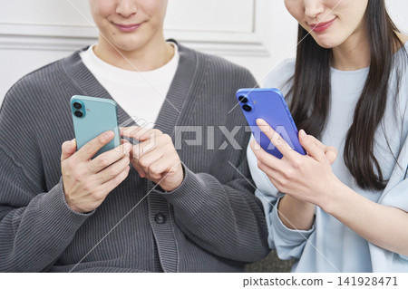 A couple using a smartphone in the living room (faceless) A couple using a smartphone in the living room (faceless) 141928471