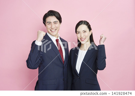 A businessman and a businesswoman making a victory pose against a pink background. A businessman and a businesswoman making a victory pose against a pink background. 141928474