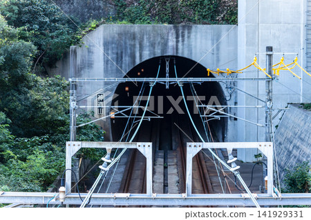 Front view of a railway tunnel and overhead line structure piercing a mountainous area. Front view of a railway tunnel and overhead line structure piercing a mountainous area. 141929331