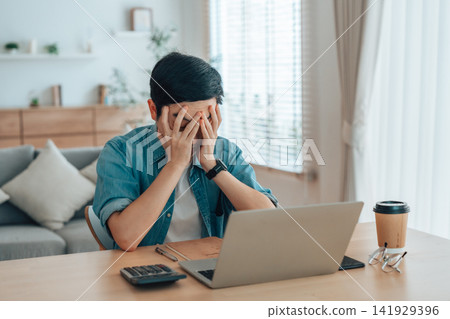 Asian man are stressed, pain in their eyes, working on laptop in living room at home Asian man are stressed, pain in their eyes, working on laptop in living room at home 141929396