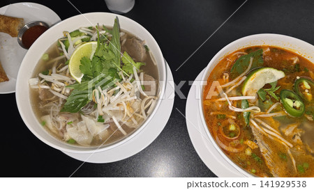 Vietnamese Pho Noodle Soup With Fresh Herbs, Lime And Crispy Spring Rolls On Table Vietnamese Pho Noodle Soup With Fresh Herbs, Lime And Crispy Spring Rolls On Table 141929538