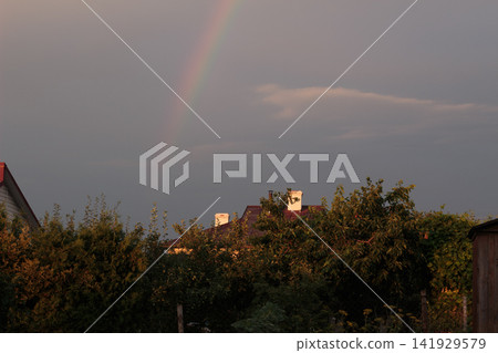 Faint Rainbow in Dark Sunset Sky over Countryside Village Roofs Faint Rainbow in Dark Sunset Sky over Countryside Village Roofs 141929579