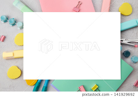 Empty white mockup on a bright variety of stationery such as pens, paper clips and notebooks scattered on a flat surface. Empty white mockup on a bright variety of stationery such as pens, paper clips and notebooks scattered on a flat surface. 141929692