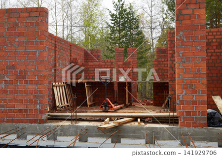 Front view of a brick construction site with pallet jack, scaffolding, and unfinished masonry walls Front view of a brick construction site with pallet jack, scaffolding, and unfinished masonry walls 141929706