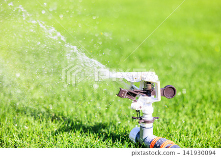 Lush green lawn and sprinkler watering on a sunny day Lush green lawn and sprinkler watering on a sunny day 141930094