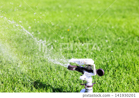 Lush green lawn and sprinkler watering on a sunny day Lush green lawn and sprinkler watering on a sunny day 141930201