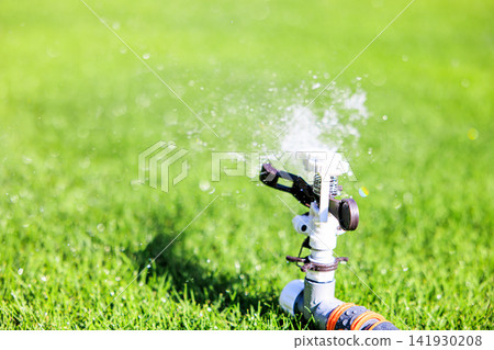 Lush green lawn and sprinkler watering on a sunny day Lush green lawn and sprinkler watering on a sunny day 141930208