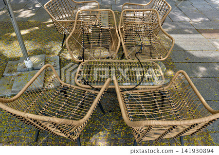 Modern wicker armchairs and glass table set on an outdoor patio covered with petals Modern wicker armchairs and glass table set on an outdoor patio covered with petals 141930894