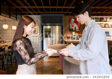 一對年輕的商務人士,一男一女,在一家時尚的咖啡廳休息室交換名片。 一對年輕的商務人士,一男一女,在一家時尚的咖啡廳休息室交換名片。 141931659