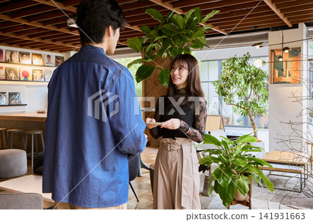 A young man and woman are talking while showing each other their smartphones in a stylish cafe. A young man and woman are talking while showing each other their smartphones in a stylish cafe. 141931663
