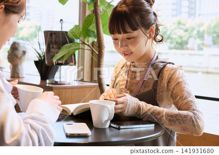 A young woman enjoying coffee while chatting with a friend at a cafe. A young woman enjoying coffee while chatting with a friend at a cafe. 141931680
