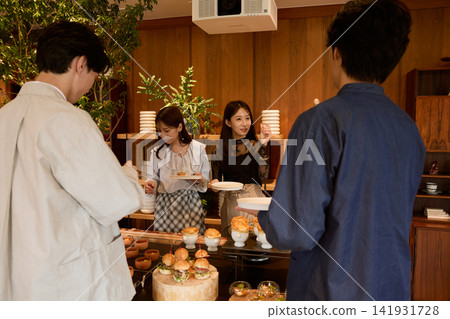 A group of young men and women enjoying buffet food at a standing reception. A group of young men and women enjoying buffet food at a standing reception. 141931728