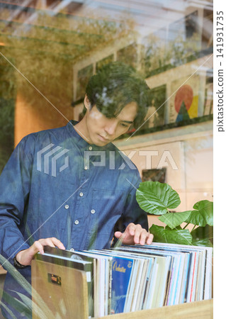 一名穿著藍色襯衫的男子正在唱片行挑選黑膠唱片。 一名穿著藍色襯衫的男子正在唱片行挑選黑膠唱片。 141931735