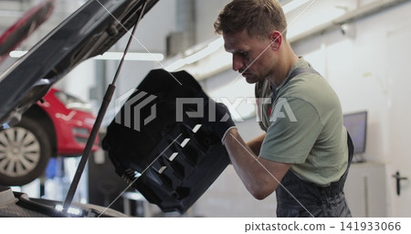 Close up of car mechanic removes the engine cover of a car and inspects the car with a lamp. Close up of car mechanic removes the engine cover of a car and inspects the car with a lamp. 141933066