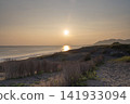The sunset reflecting on the shoreline and the silhouette of the coastline 141933094
