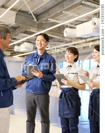 Staff members chatting with the manager who is holding a tablet. 141933190