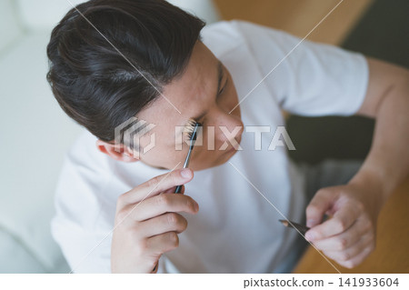 A man's eyebrow makeup using an eyebrow brush and pencil, filmed from an overhead angle. A man's eyebrow makeup using an eyebrow brush and pencil, filmed from an overhead angle. 141933604