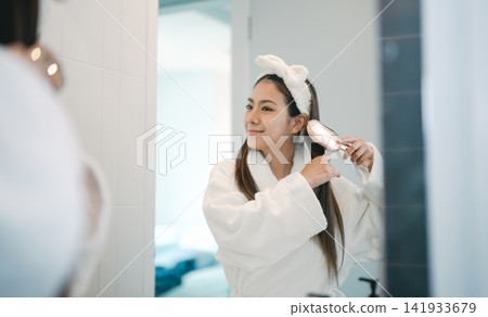 Asian woman combing hair in front of a mirror in bathroom getting ready in a morning hairbrush Asian woman combing hair in front of a mirror in bathroom getting ready in a morning hairbrush 141933679