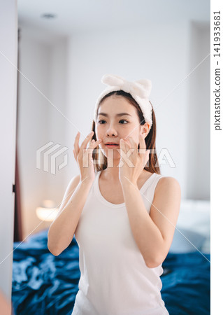 Asian woman applying a eye facial sheet mask in bedroom skincare and wellness morning routine Asian woman applying a eye facial sheet mask in bedroom skincare and wellness morning routine 141933681