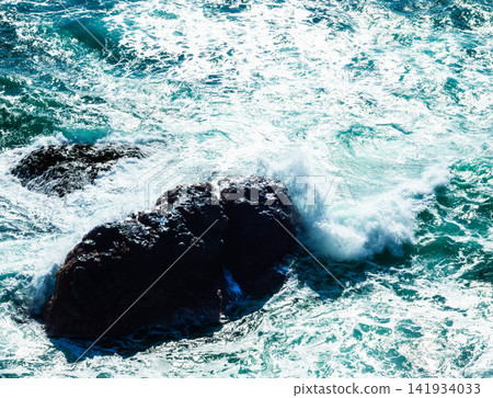 A view of the rocky reefs and the rough sea with white waves from atop a cliff. A view of the rocky reefs and the rough sea with white waves from atop a cliff. 141934033