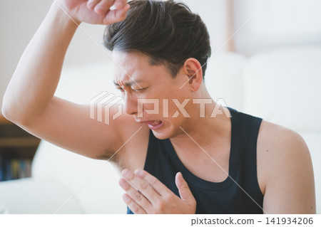 A 40-year-old man checks his underarm odor by fanning himself with his hand and sniffing his armpits. A 40-year-old man checks his underarm odor by fanning himself with his hand and sniffing his armpits. 141934206