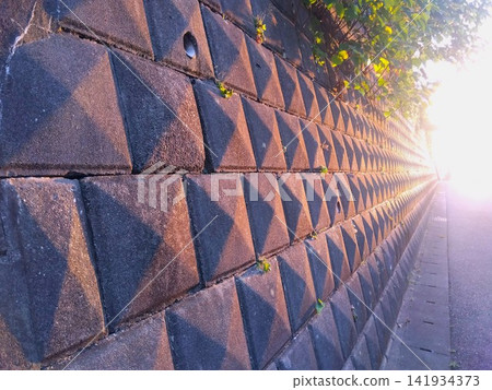 A view of a retaining wall of a hilltop house bathed in the setting sun on a summer evening. A view of a retaining wall of a hilltop house bathed in the setting sun on a summer evening. 141934373