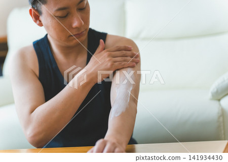 A 40-year-old man applies cream to his entire arm as part of his men's body skincare routine. A 40-year-old man applies cream to his entire arm as part of his men's body skincare routine. 141934430