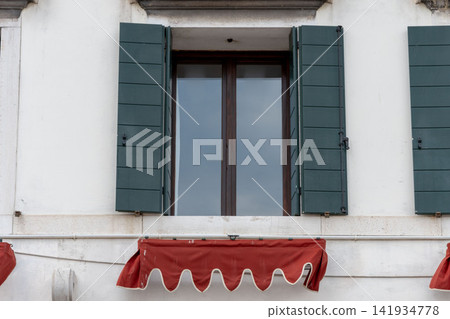 Open green shutters framing a tall window above red awning 141934778