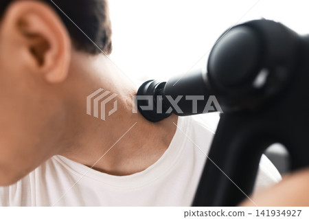 man uses a massage gun on his neck for percussion therapy and myofascial release, providing self care to relieve muscle tension and aid recovery. man uses a massage gun on his neck for percussion therapy and myofascial release, providing self care to relieve muscle tension and aid recovery. 141934927