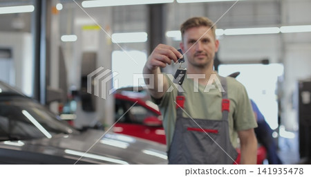Auto mechanic showing car keys at camera. Smiling Caucasian man posing at workplace in repair shop. Automotive industry, auto care, service. Auto mechanic showing car keys at camera. Smiling Caucasian man posing at workplace in repair shop. Automotive industry, auto care, service. 141935478